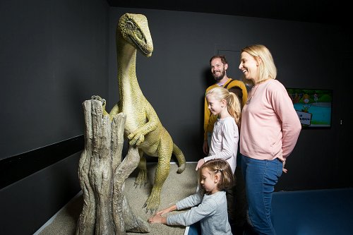 Družina na ogledu Centra za obiskovalce Geoparka Idrija pred maketo dinozavra.